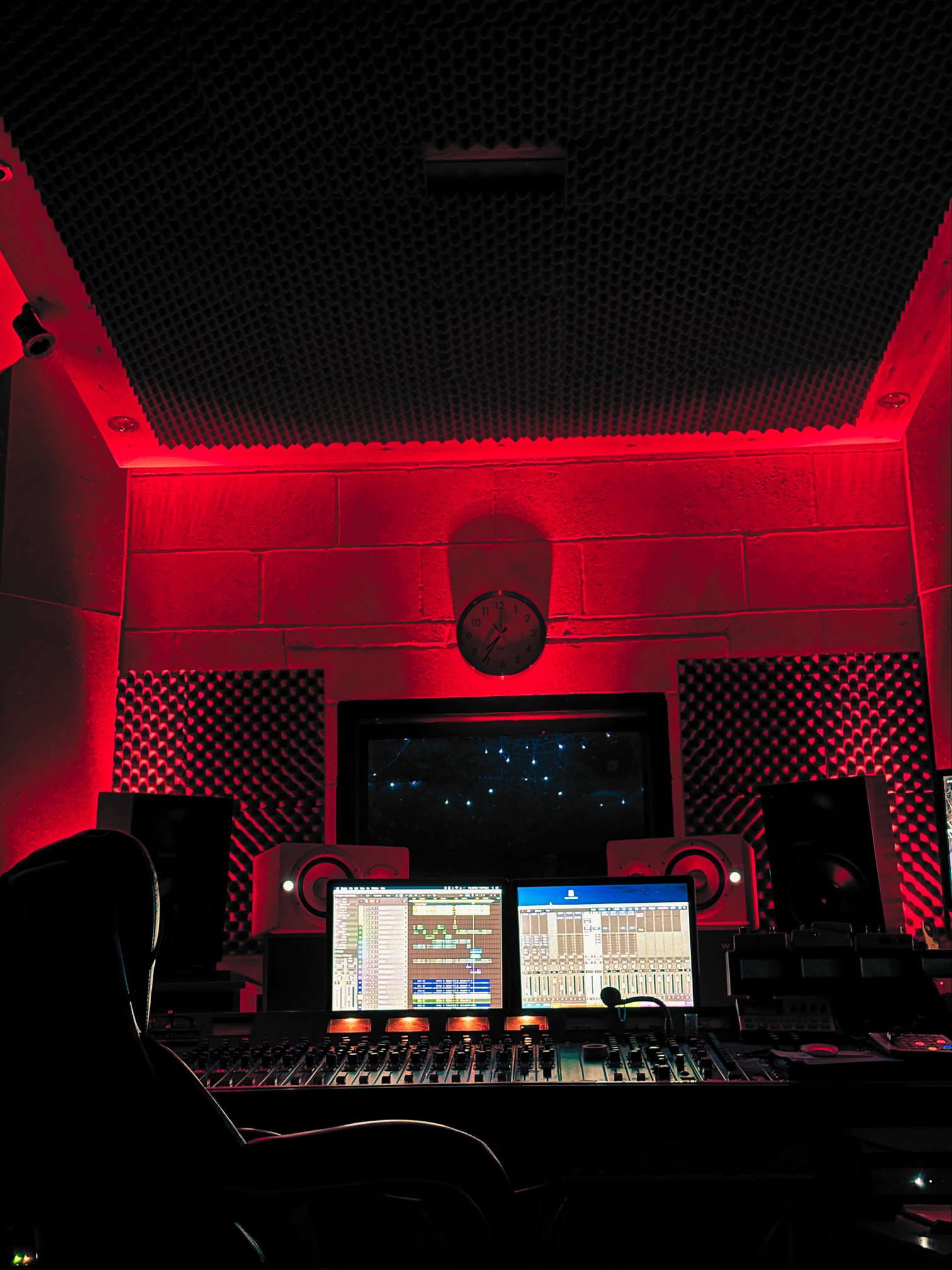 The control room at VIBE Recording Studio in Manchester. Bold red lights cast shadows over the dark vintage mixing desk, the bright white glow of the two screens illuminate every pot, switch, fader and button.